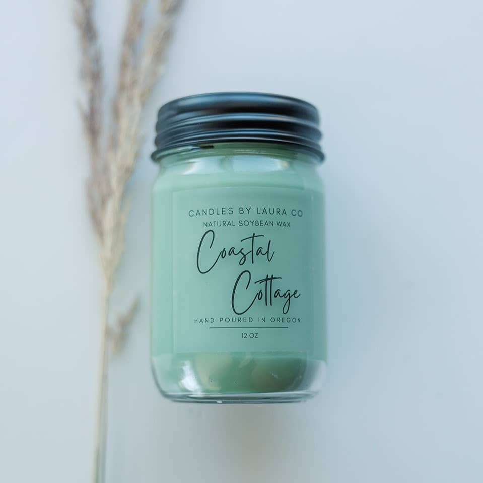 A teal candle in a glass jar, labeled “Coastal Cottage”.