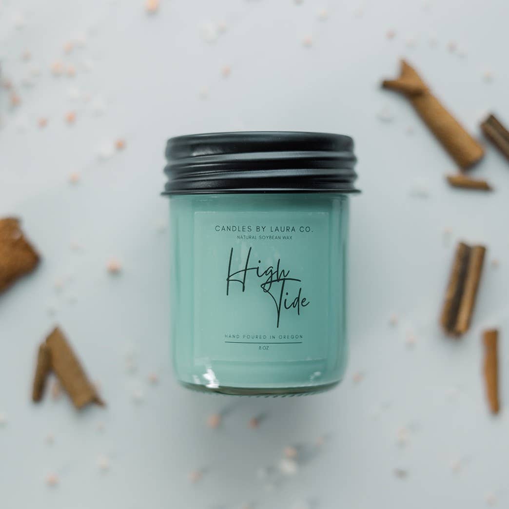 An image of a teal candle in a glass jar with a black lid, labelled “High Tide.”