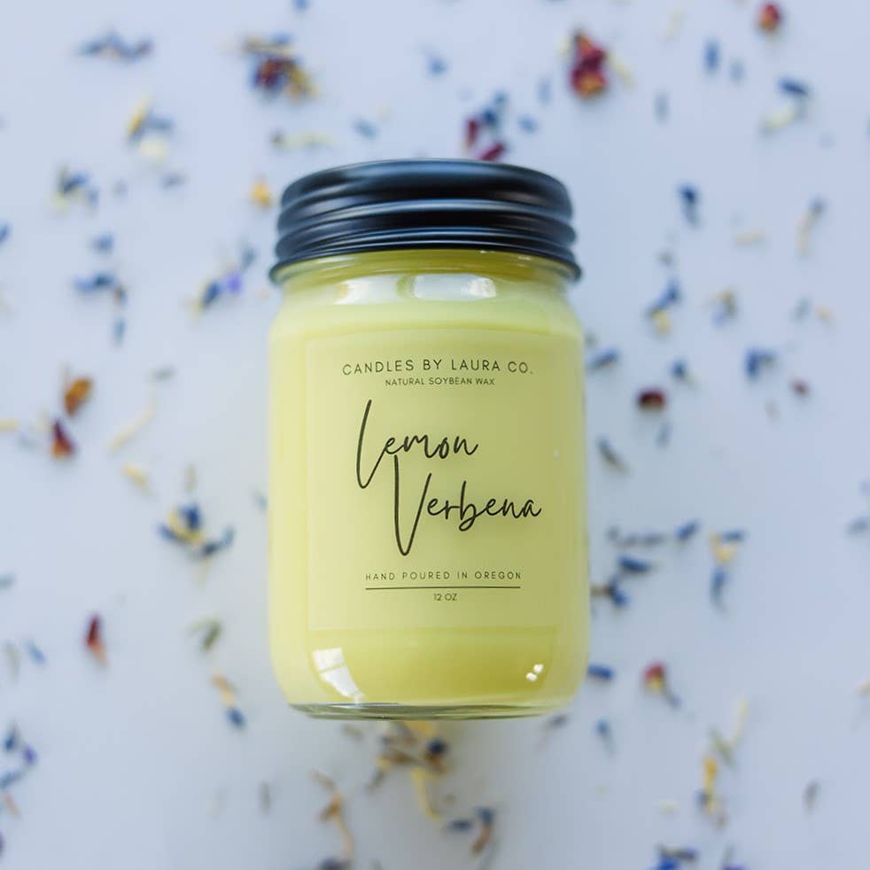 A yellow candle in a glass jar labeled “Lemon Verbena”.