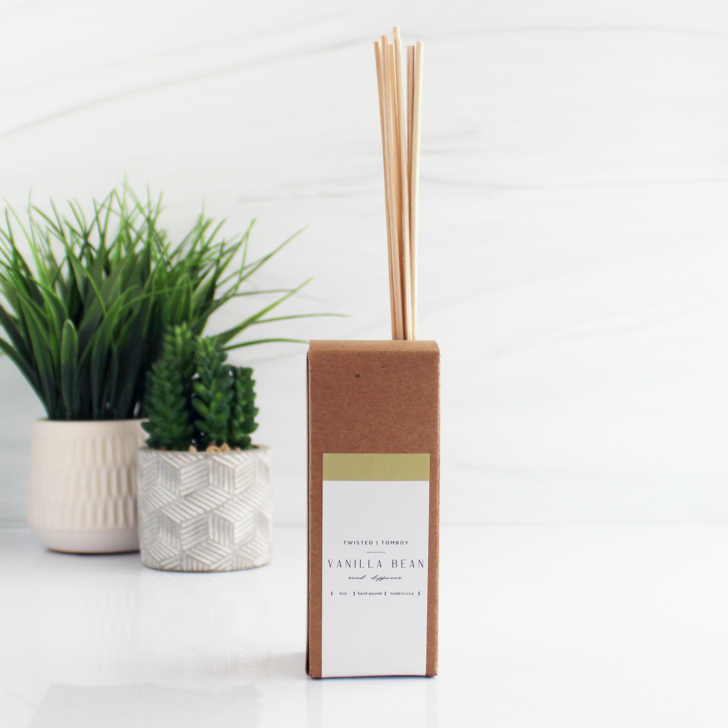 A cardboard box with reeds sticking out of it, labeled “Vanilla Bean Reed Diffuser”.