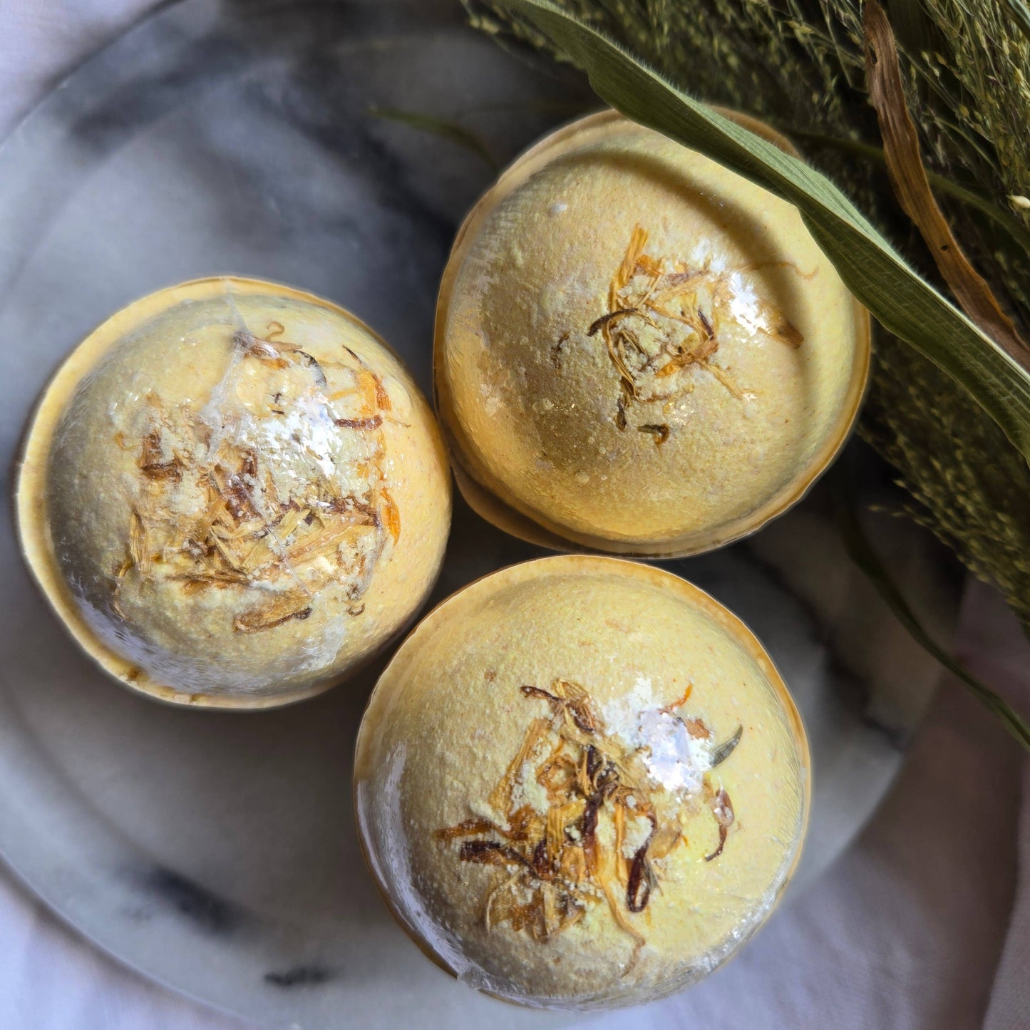 A trio of Sun Dancer bath bombs, pastel yellow bath bombs topped with dried citrus.
