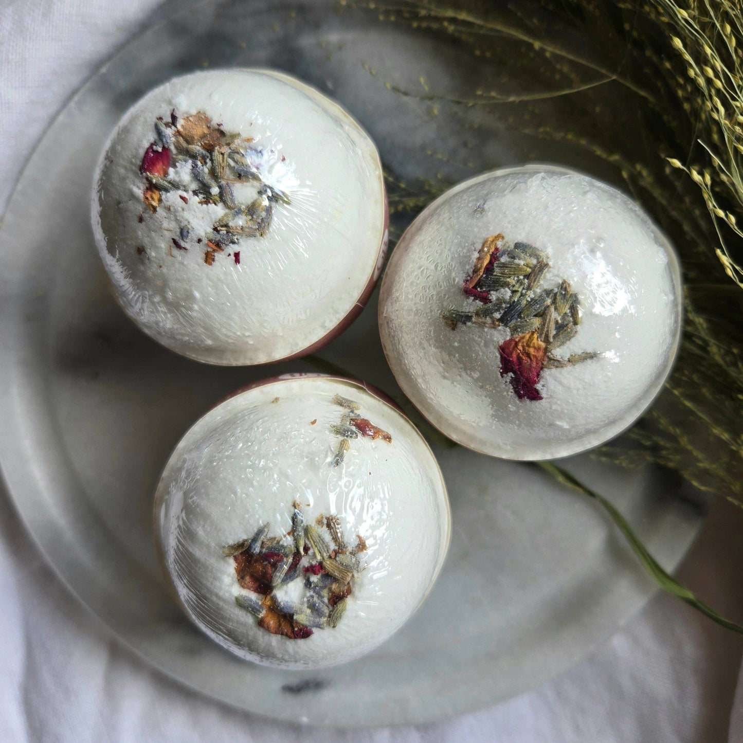 A trio of The Dreamer bath bombs, white bath bombs topped with fragments of rose, lavender, and cedarwood.
