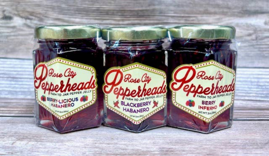 Three jars of Rose City Pepperheads jelly on a wooden surface