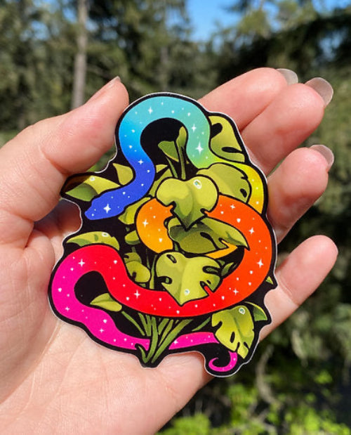 Colorful sticker with a snake and leaves held in a hand against a blurred natural background