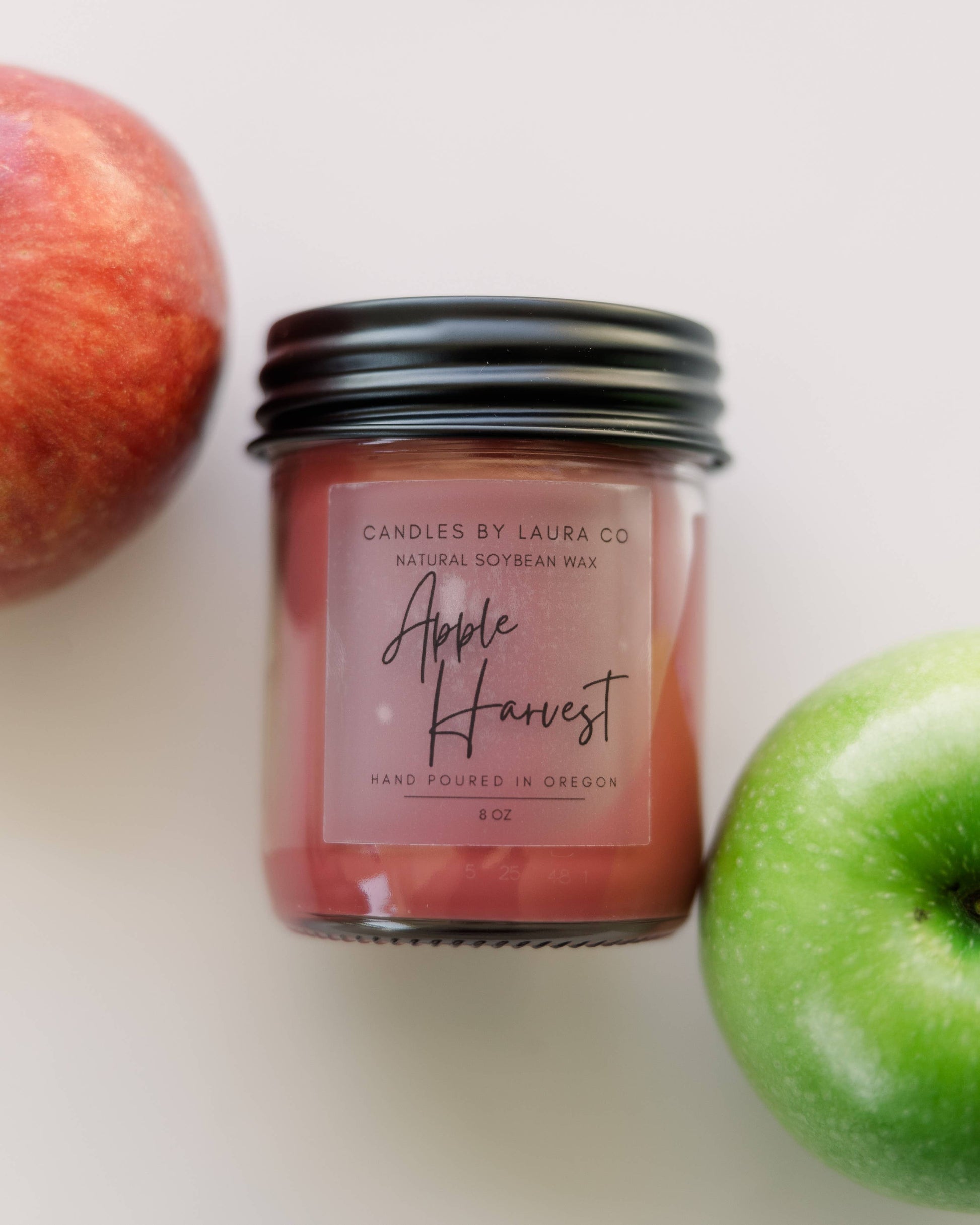 Image of the Apple Harvest candle, a red candle in a jar with a black lid.