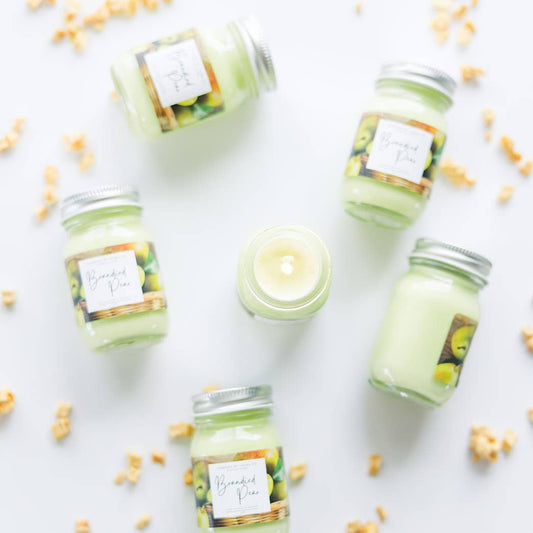 Image of six Brandied Pear candles, pastel  green candles in miniature mason jars. One is open and lit, while the other five are arrayed around it.