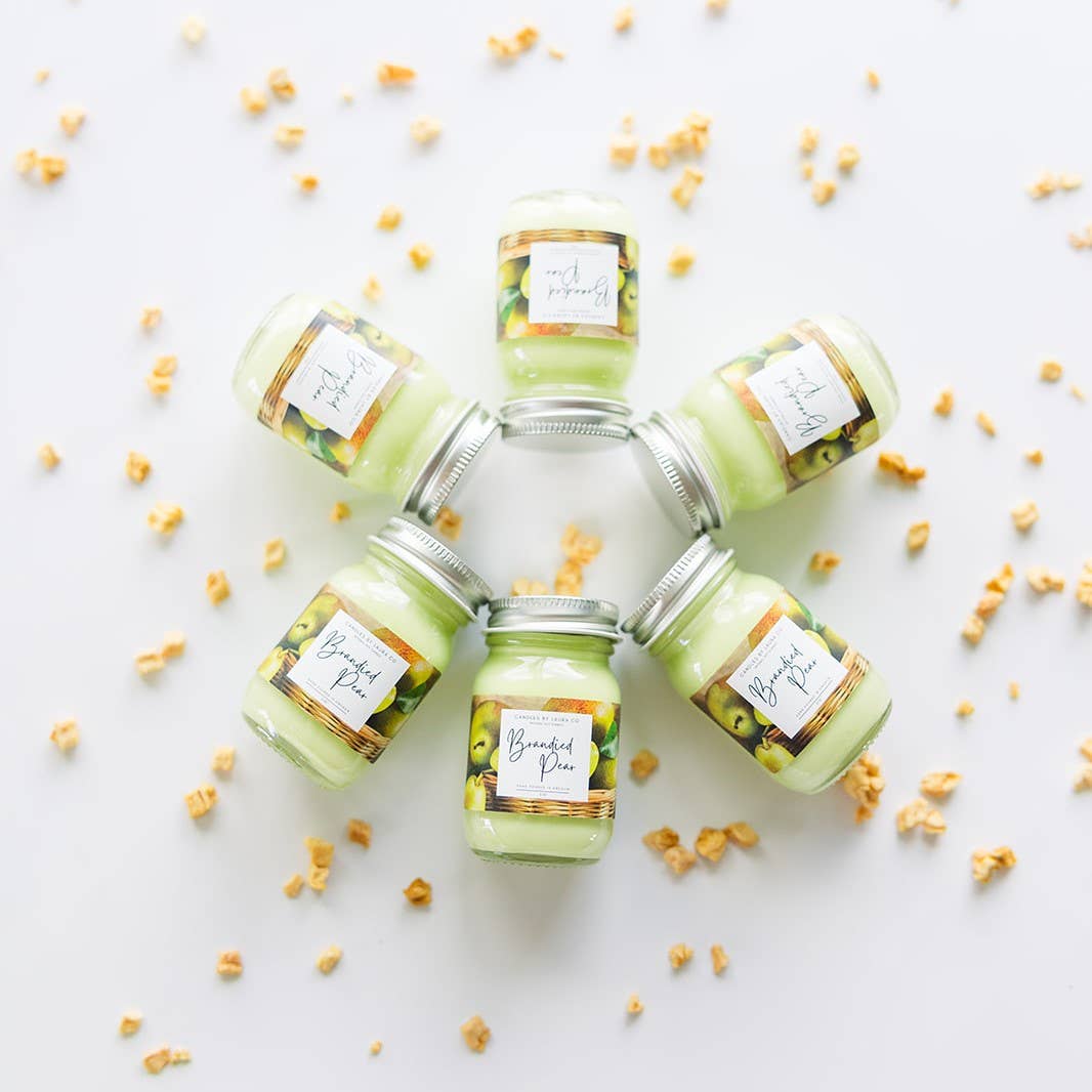 Image of six Brandied Pear candles, pastel green candles in miniature mason jars, laid out in a circle.