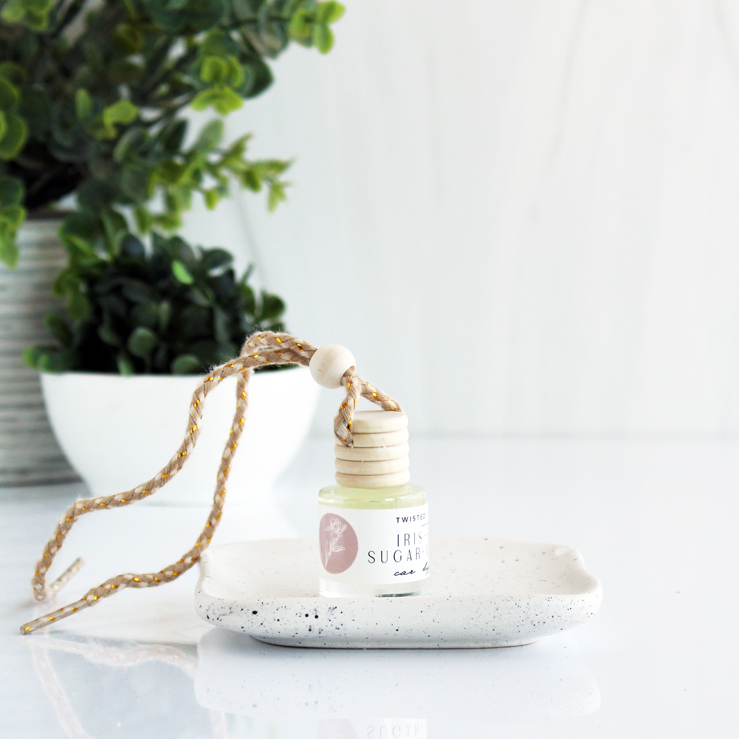 A small bottle of clear liquid with a cord attached to the lid allowing it to be hung up. The bottle is rotated at an angle that doesn’t allow the full label to be read, but the words “Iris” and “Sugar” are visible.