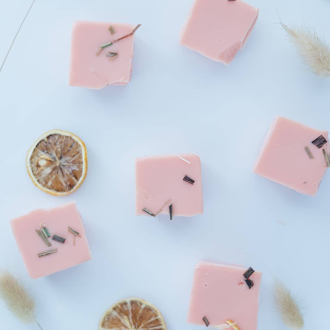 Image of the six pieces of the Citrus Agave wax melt broken apart, individual squares of pink wax topped with lemongrass and dried citrus fruit, scattered across a table.