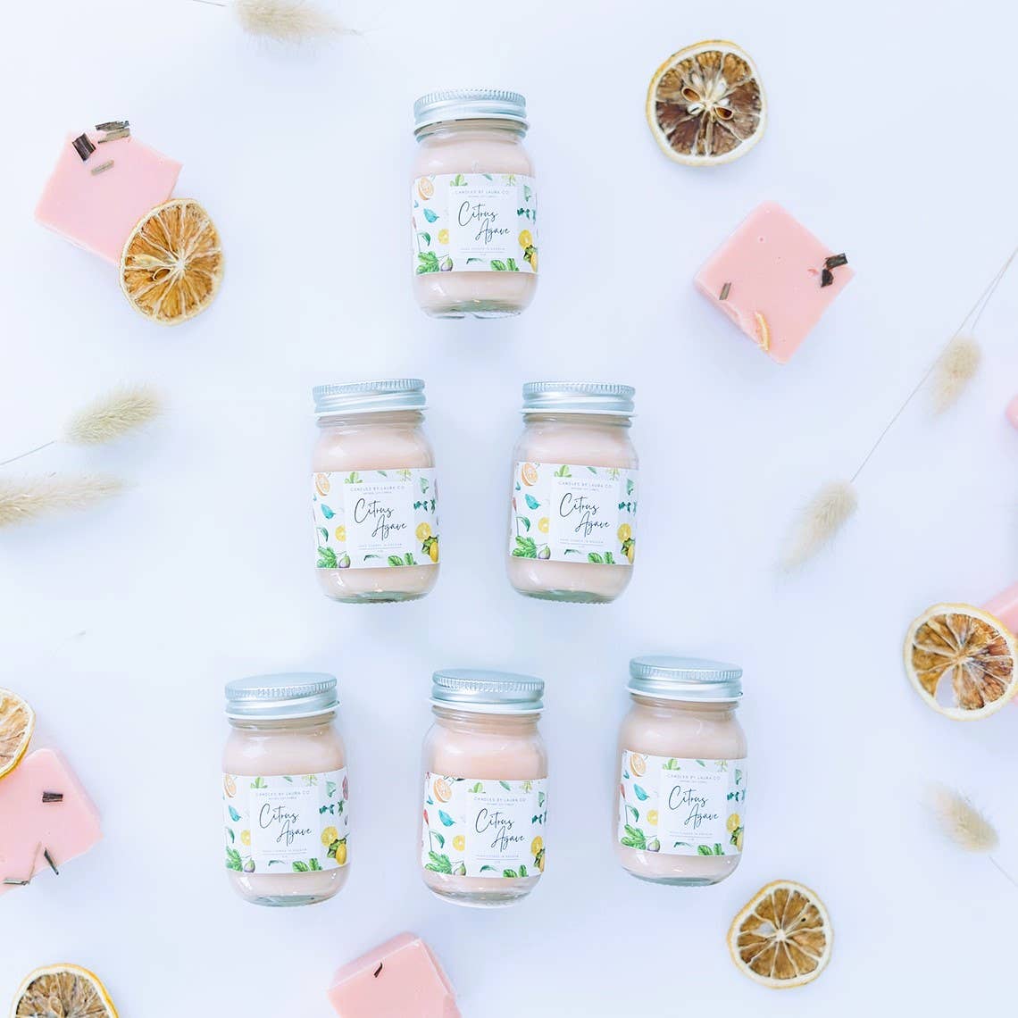 Image of six Citrus Agave candles, pale pink candles in miniature mason jars, laid out in a pyramid shape.