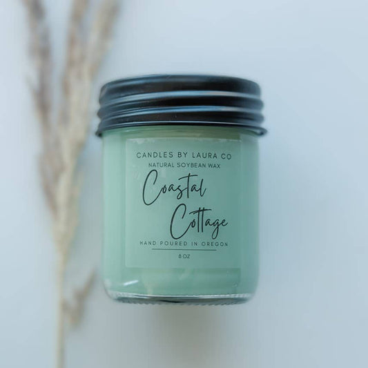 A teal candle in a glass jar, labeled “Coastal Cottage”.