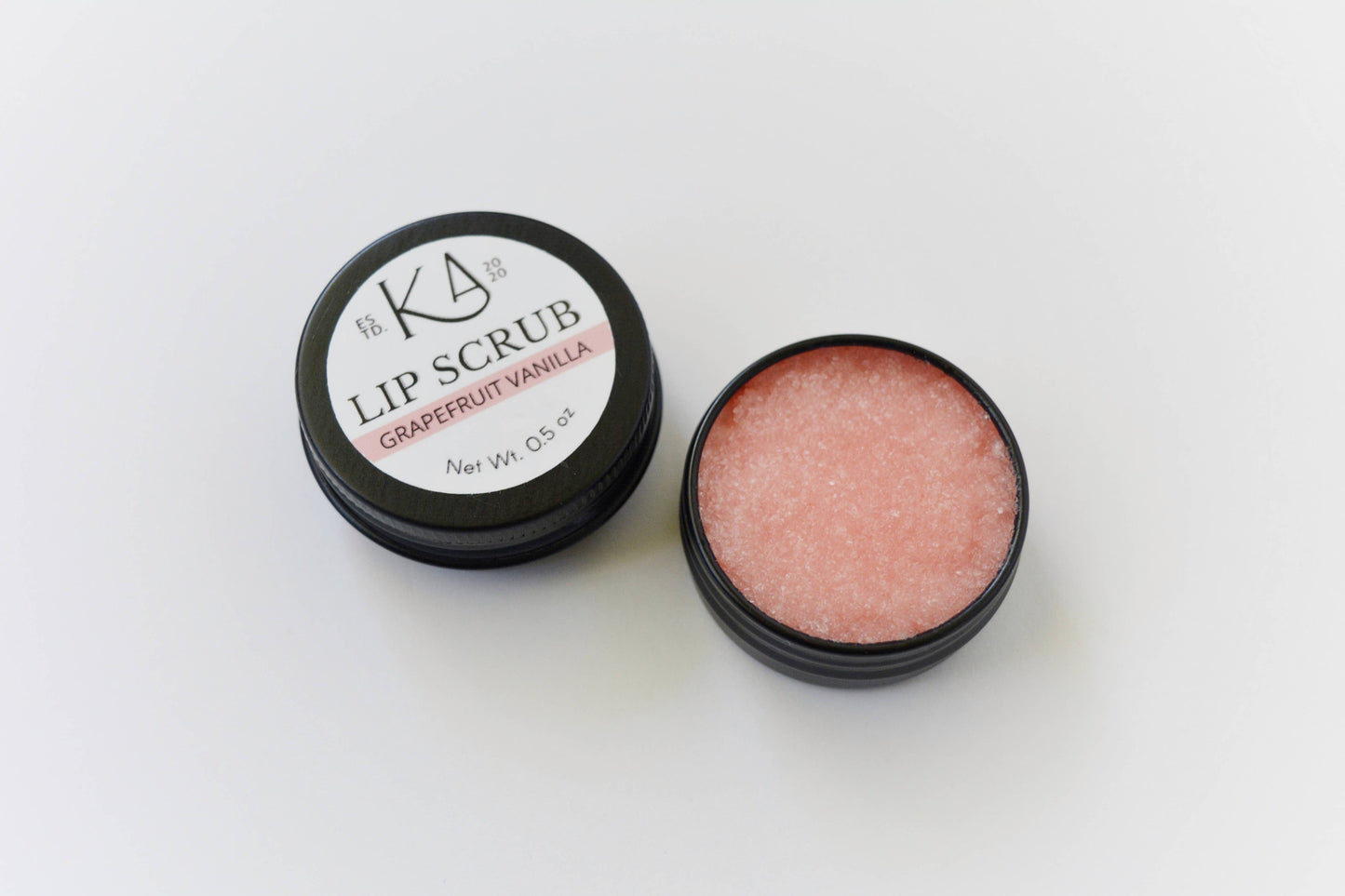 Shows the grapefruit vanilla lip scrub, cracked open to reveal the pastel red scrub inside.