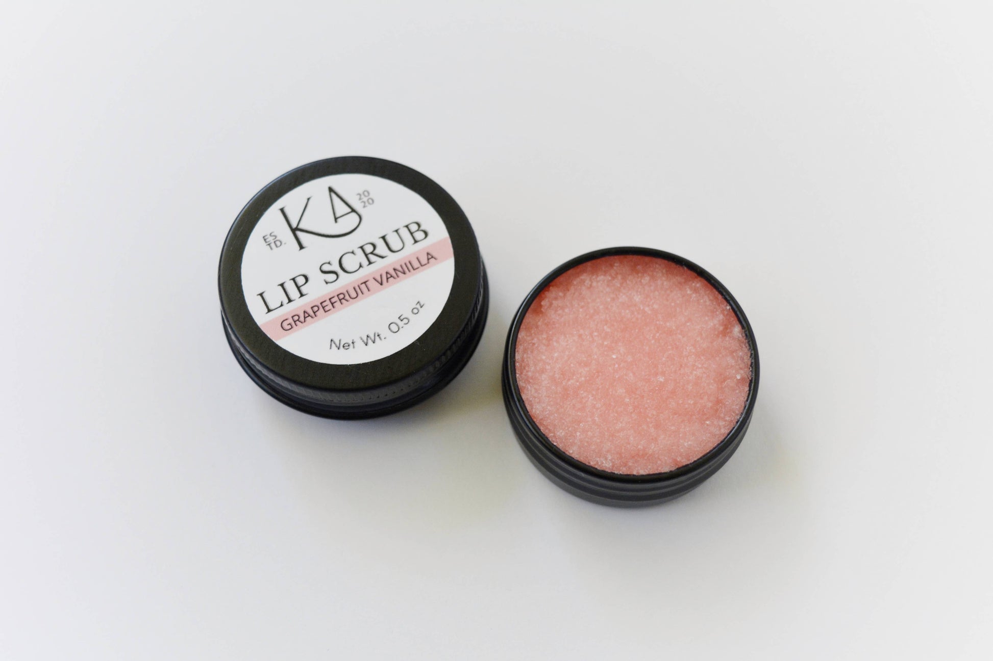 Shows the grapefruit vanilla lip scrub, cracked open to reveal the pastel red scrub inside.