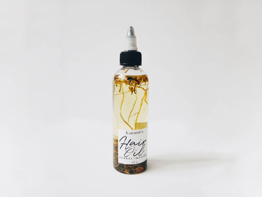 Shows the hair oil against a white background. It’s a yellowish oil with various small herbs and fragments of plants floating in it.