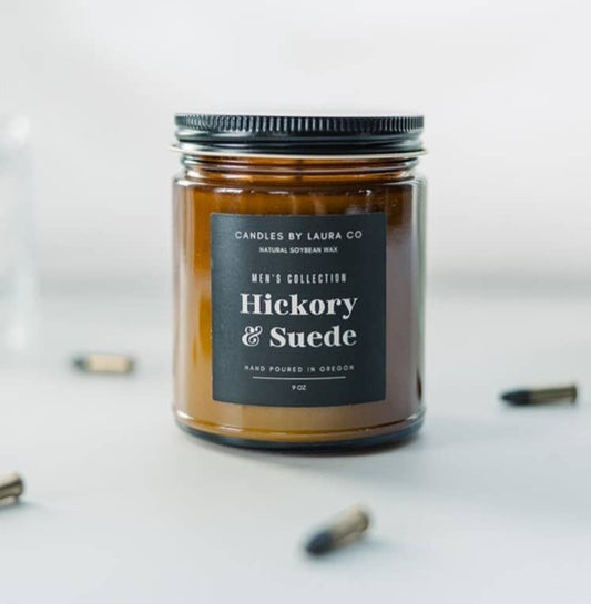 A candle in an amber-tinted mason jar, labeled “Hickory & Suede”.