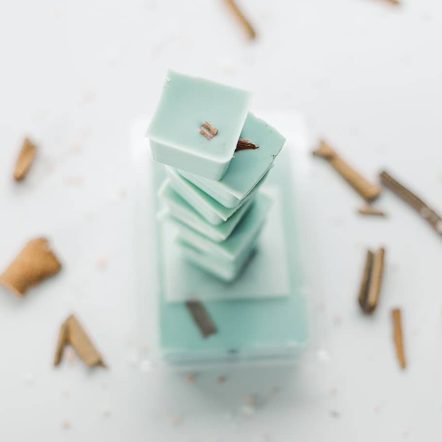 Image of the six individual blocks of wax that make up a High Tide wax melt, broken apart and stacked on top of a whole wax melt; the High Tide wax melt is blue wax with pieces of cinnamon stick suspended in it.