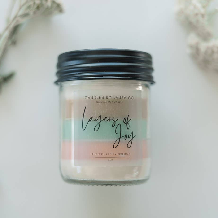 Image showing the Layers Of Joy candle; this one is five-layered, with pastel layers from top to bottom - white, tan, mint green, pink, white. The candle is in a jar with a black lid.