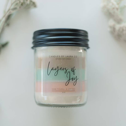 Image showing the Layers Of Joy candle; this one is five-layered, with pastel layers from top to bottom - white, tan, mint green, pink, white. The candle is in a jar with a black lid.