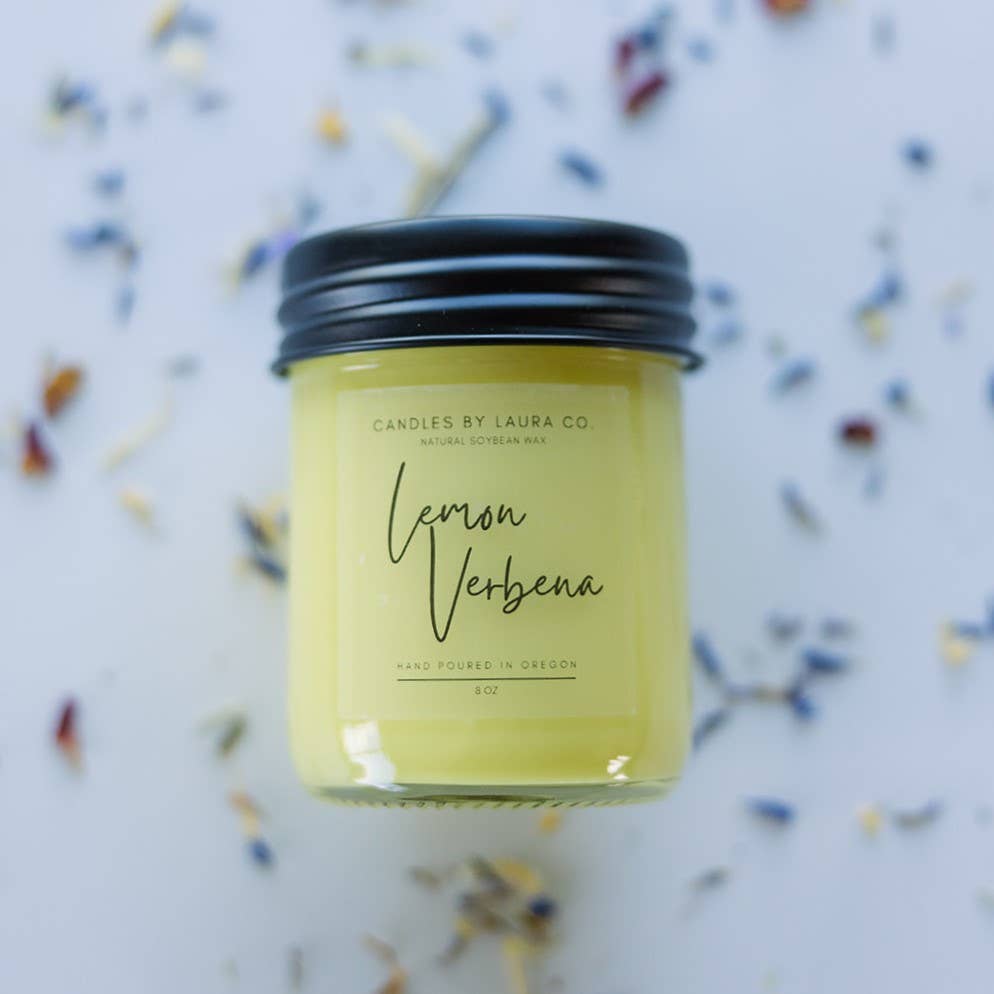 A yellow candle in a glass jar labeled “Lemon Verbena”.