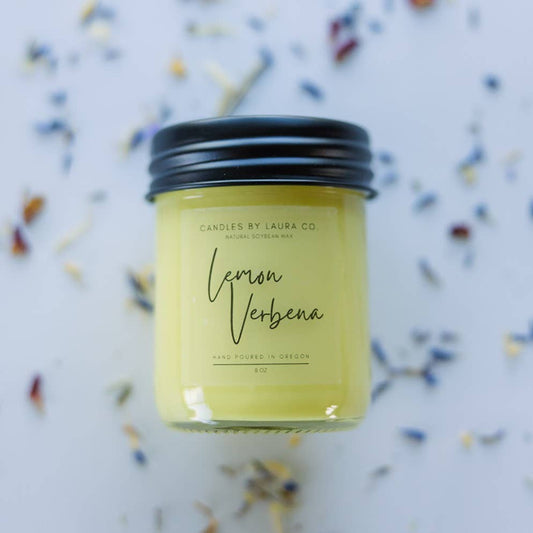 A yellow candle in a glass jar labeled “Lemon Verbena”.