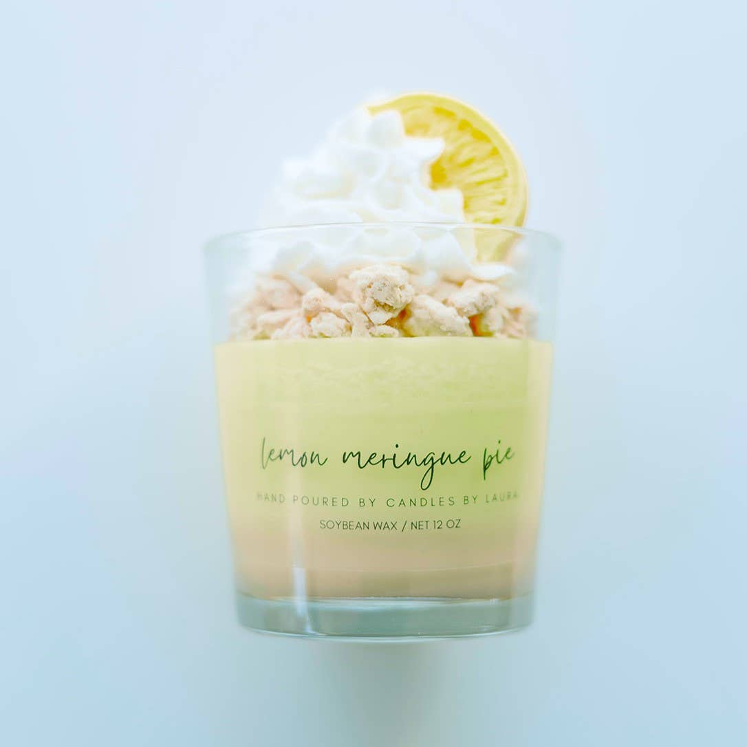 Image of a candle in a clear glass jar. The bottom layer of the candle is beige wax, and the upper layer is a pastel yellow. The candle is topped with decorations of crumbled pastry, whipped cream, and a slice of lemon, all sculpted from wax.