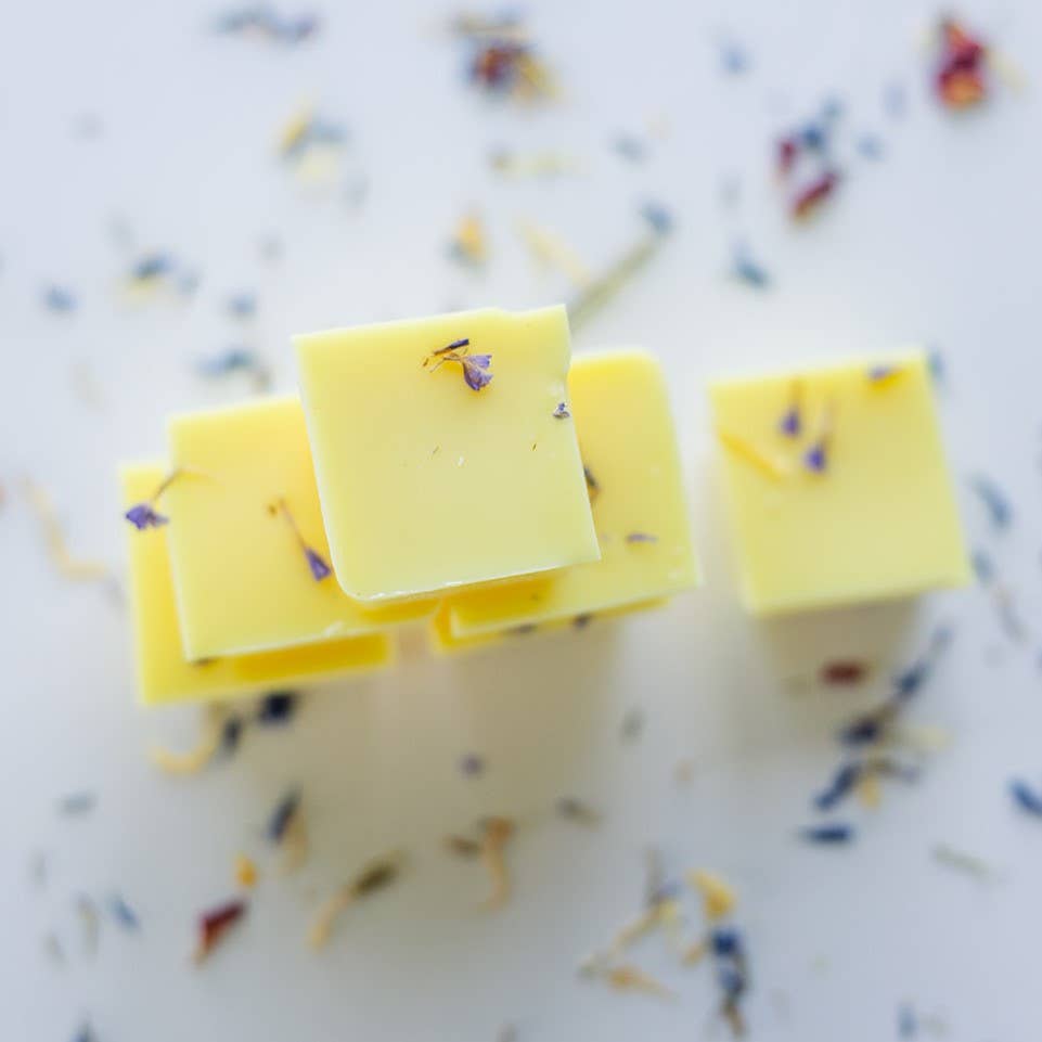 Image of the Lemon Verbena wax melt, a yellow wax with limonium petals suspended in it, broken into six individual blocks and stacked in a pyramid.