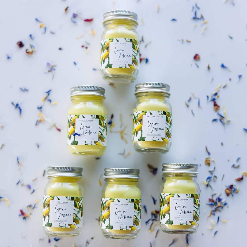 Image of six Lemon Verbena candles, yellow candles in miniature mason jars, laid out in a pyramid shape;.