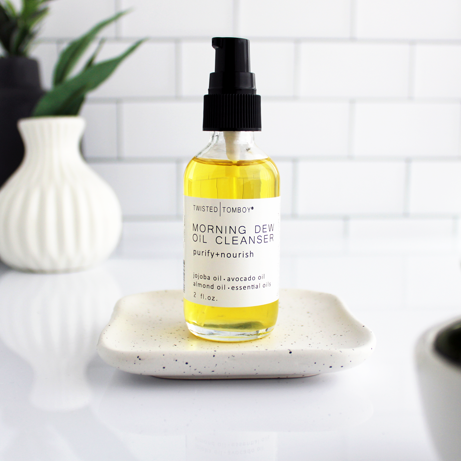 A glass bottle of yellow liquid with a pump lid. The bottle is labeled “Morning Dew Oil Cleanser - purify+nourish”.