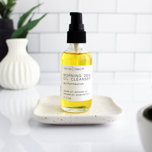 A glass bottle of yellow liquid with a pump lid. The bottle is labeled “Morning Dew Oil Cleanser - purify+nourish”.