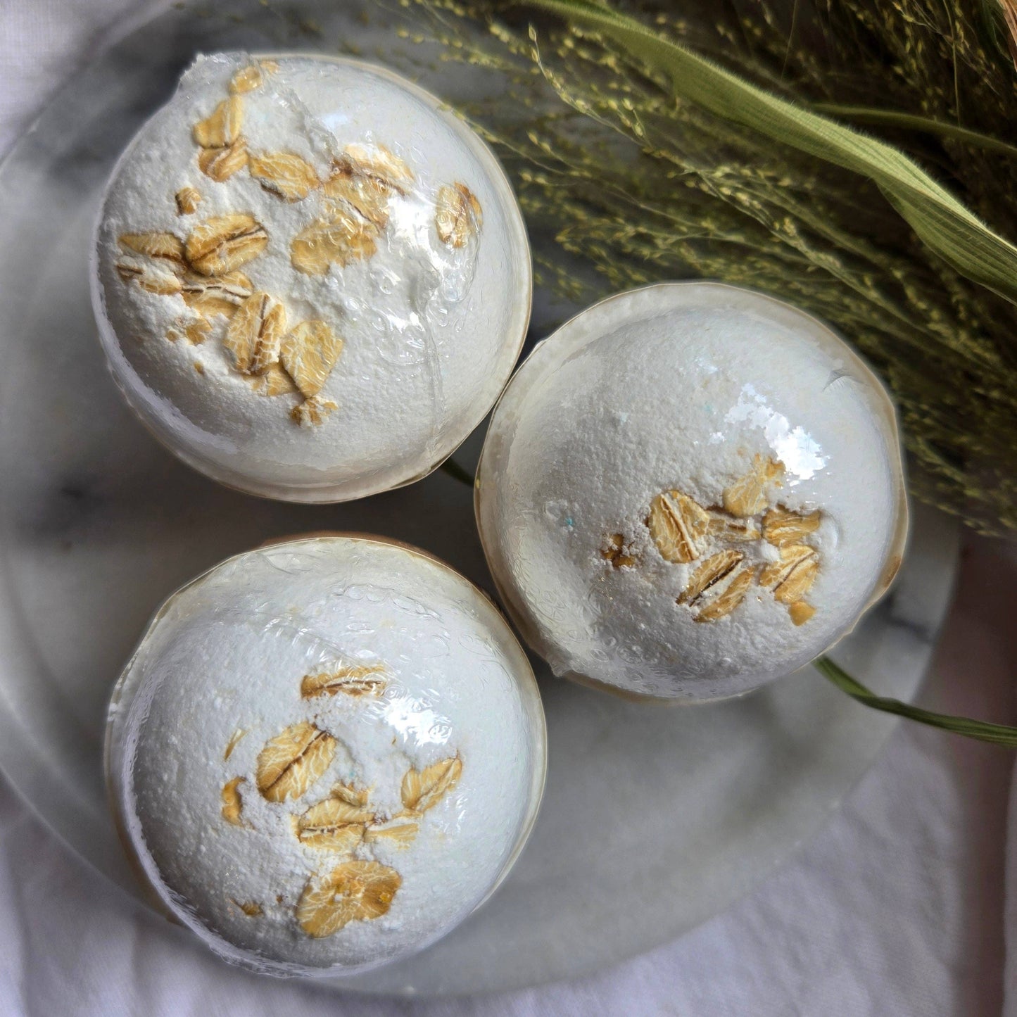 A trio of Oat & Honey bath bombs, which are white bath bombs topped with oats.