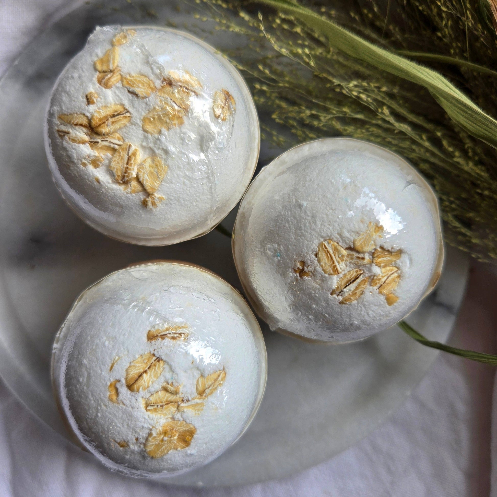A trio of Oat & Honey bath bombs, which are white bath bombs topped with oats.
