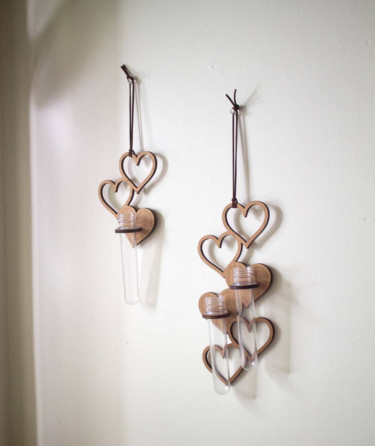Two propagation stations. Each one is a series of hanging wooden hearts, with a wooden ring holding up clear test tubes. The propagation station on the right has two tubes, and the propagation station on the left has one.