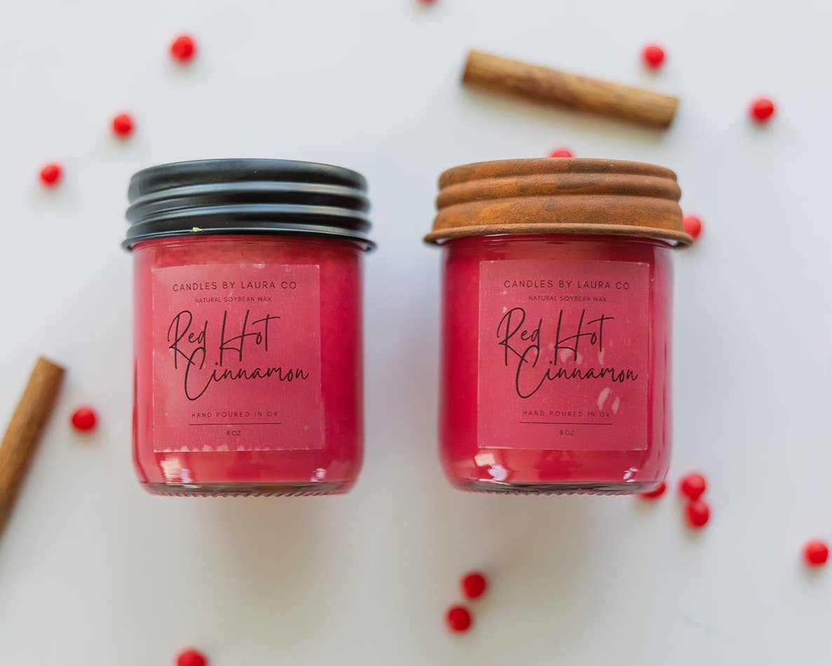 A pair of red candles in glass jars, labeled “Red Hot Cinnamon”.