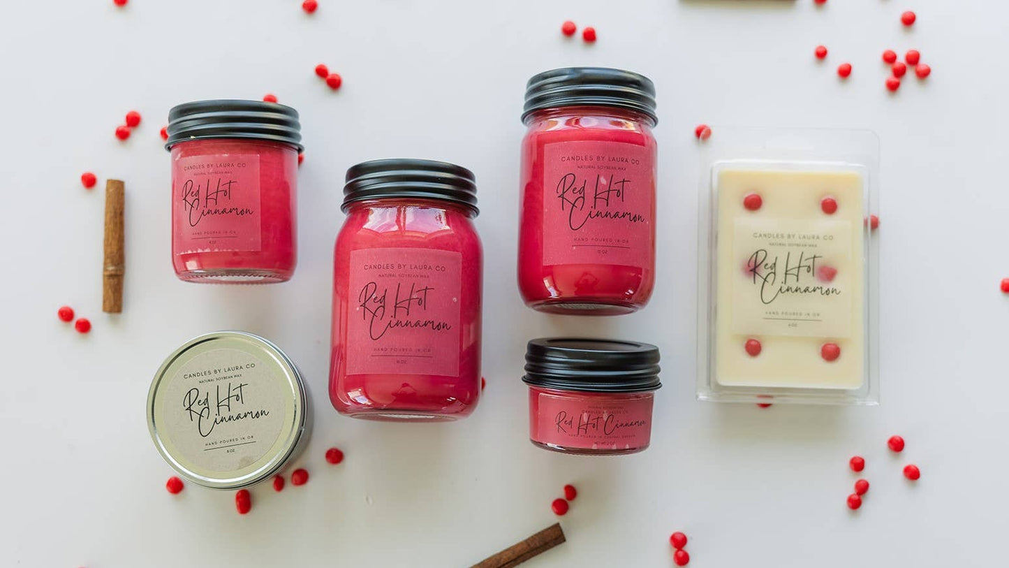 A variety of red candles in different sized jars, and a white wax melt decorated with red dots, all labeled “Red Hot Cinnamon”.