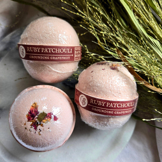 A trio of Ruby Patchouli bath bombs, which are pale pink bath bombs topped with flower petals.