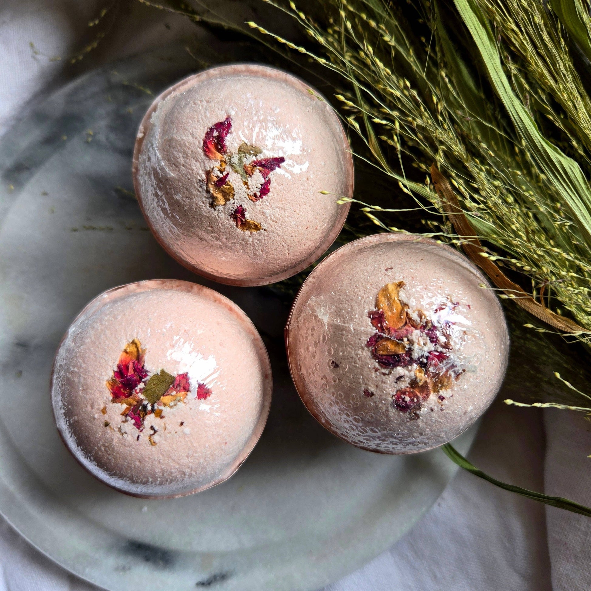 A trio of Ruby Patchouli bath bombs, which are pale pink bath bombs topped with flower petals.
