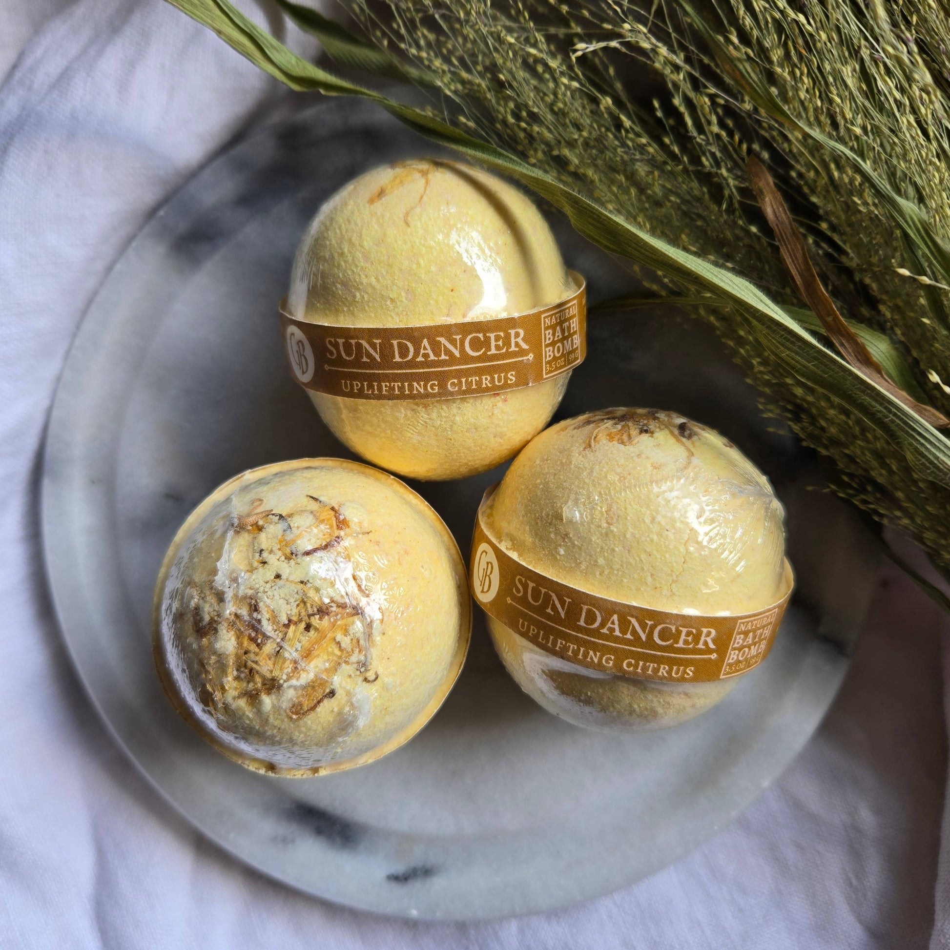 A trio of Sun Dancer bath bombs, pastel yellow bath bombs topped with dried citrus.