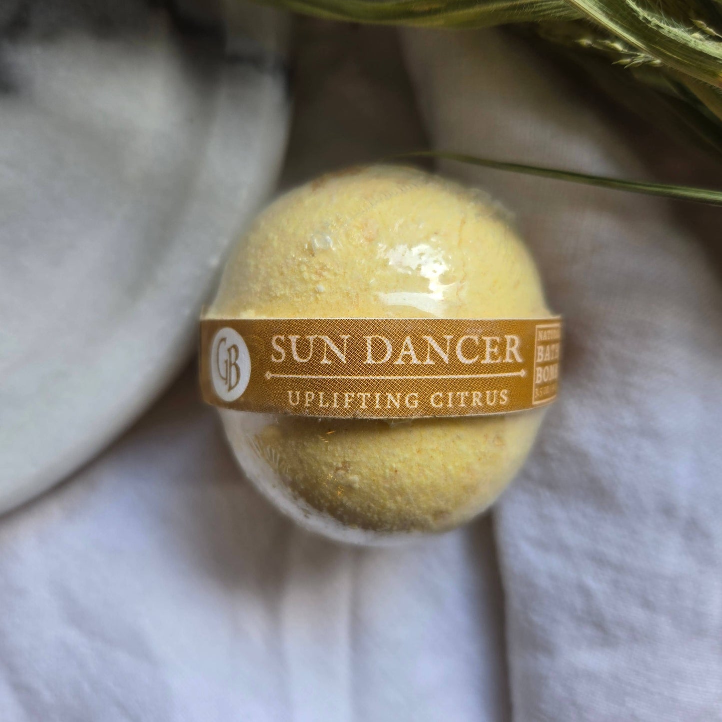 A pastel yellow bath bomb labeled as “Sun Dancer” with the tagline “Uplifting Citrus”.