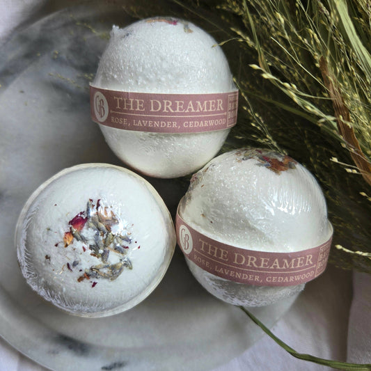 A trio of The Dreamer bath bombs, white bath bombs topped with fragments of rose, lavender, and cedarwood.