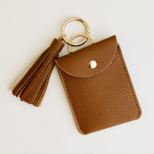 Brown leather cardholder with tassel and gold ring on a light beige background