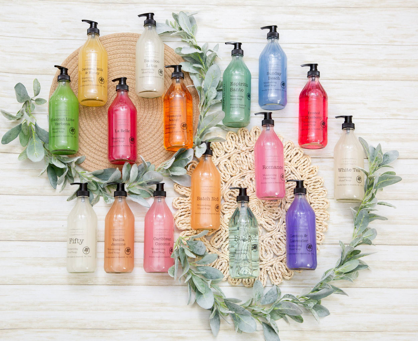 Multiple pump bottles of hand soap in various colors arranged in a aesthetic display with green leaves.