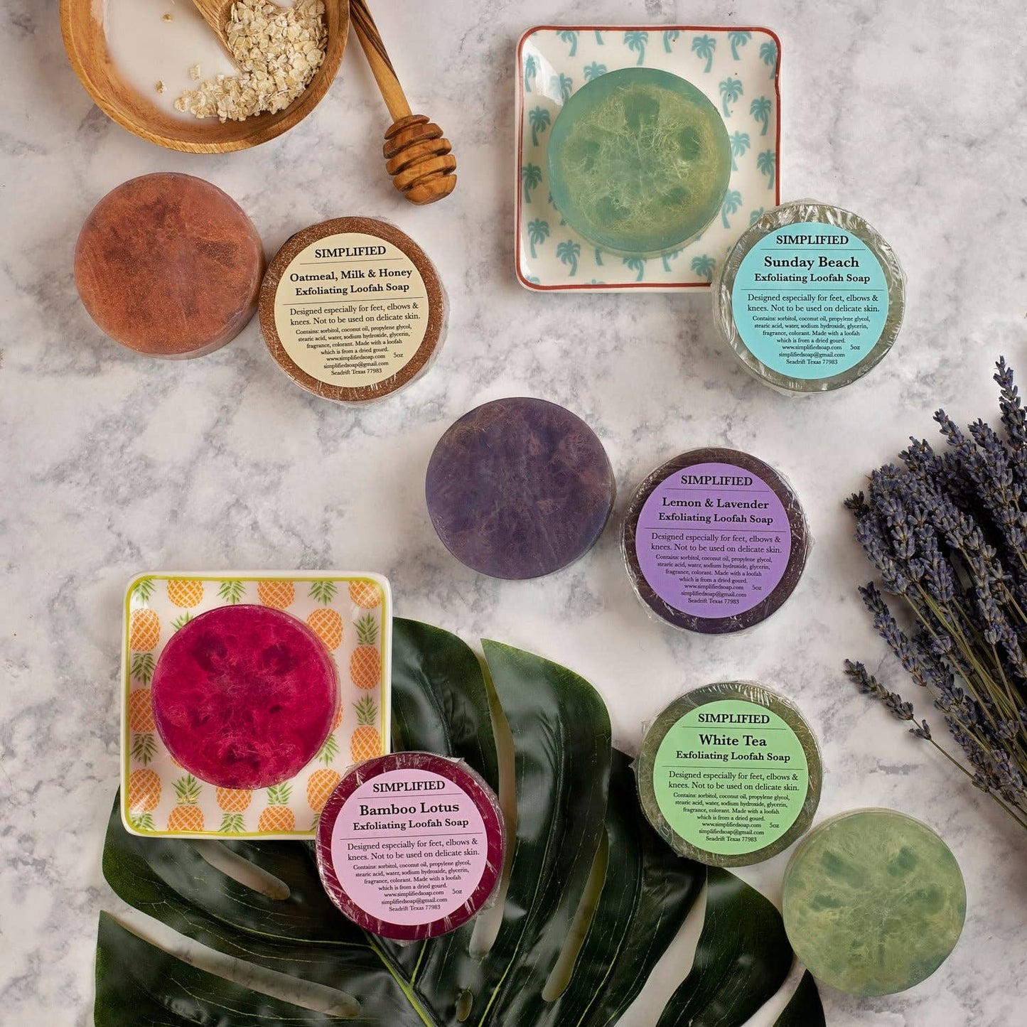 Collection of various loofah soaps and containers on a textured surface with plants and honeycomb.
