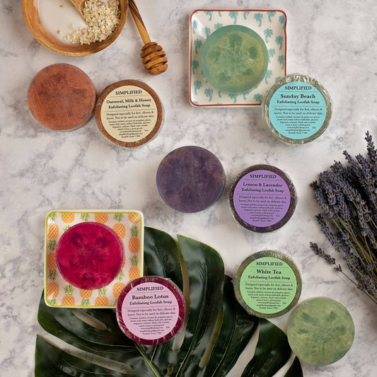 Collection of various loofah soaps and containers on a textured surface with plants and honeycomb.